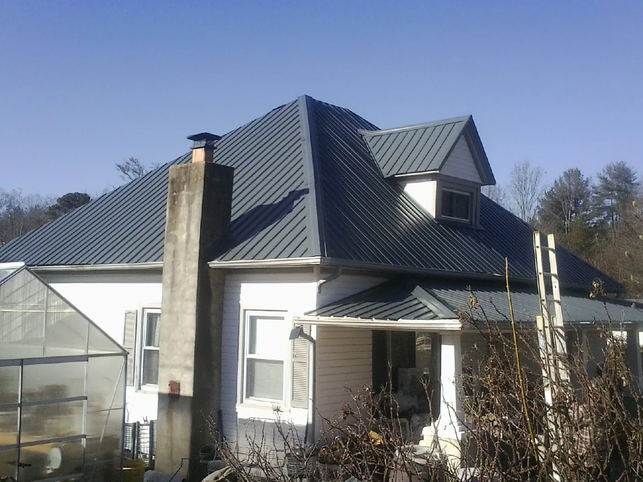Dark blue standing seam metal roof on a white farmhouse with dormer — Slate & Tile Roof Repair by Roofing Brothers in Moffit