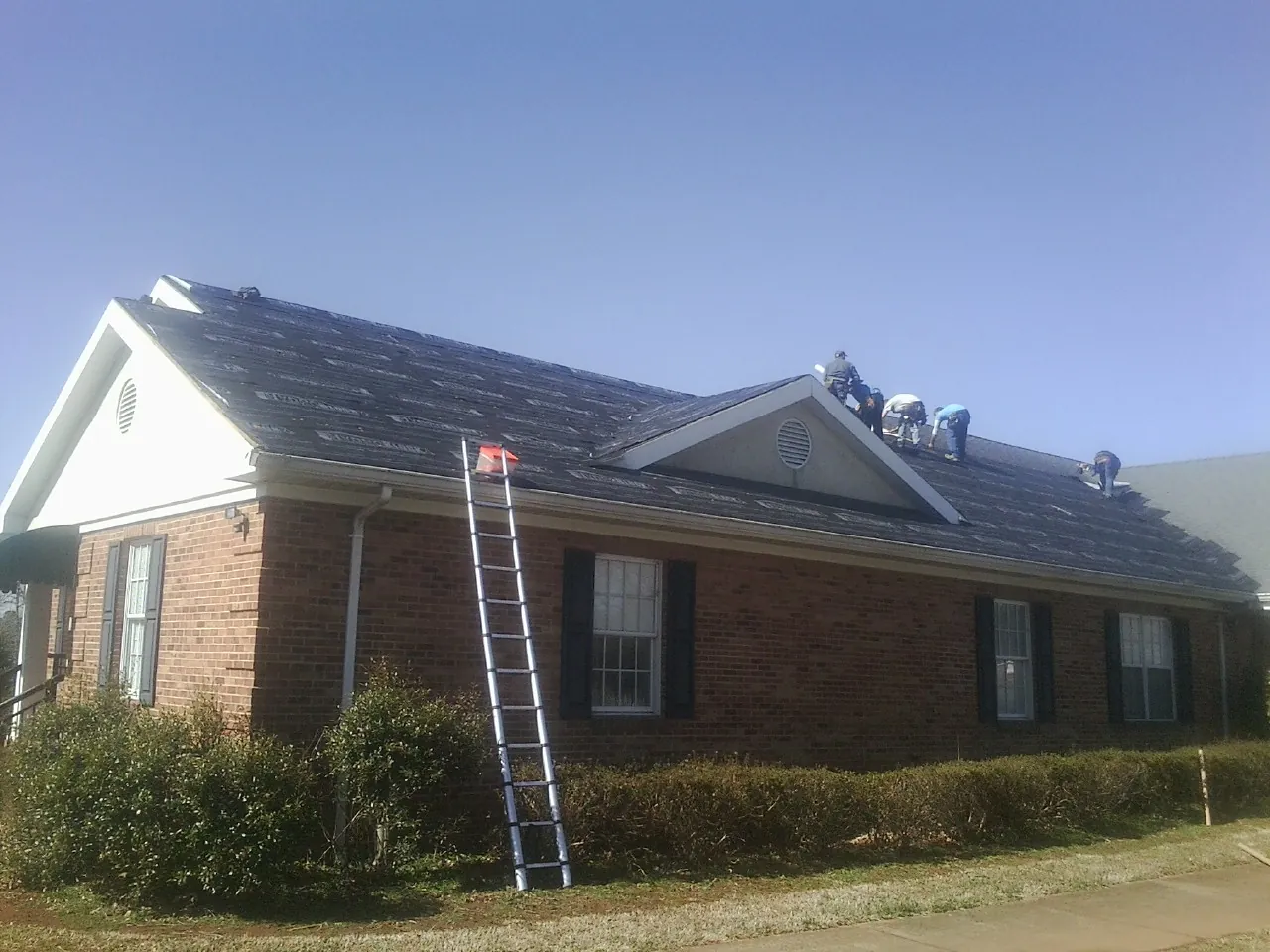 Crew tearing shingles off a brick ranch roof with a ladder set — Metal Roof Repair work by our crew in Moffit