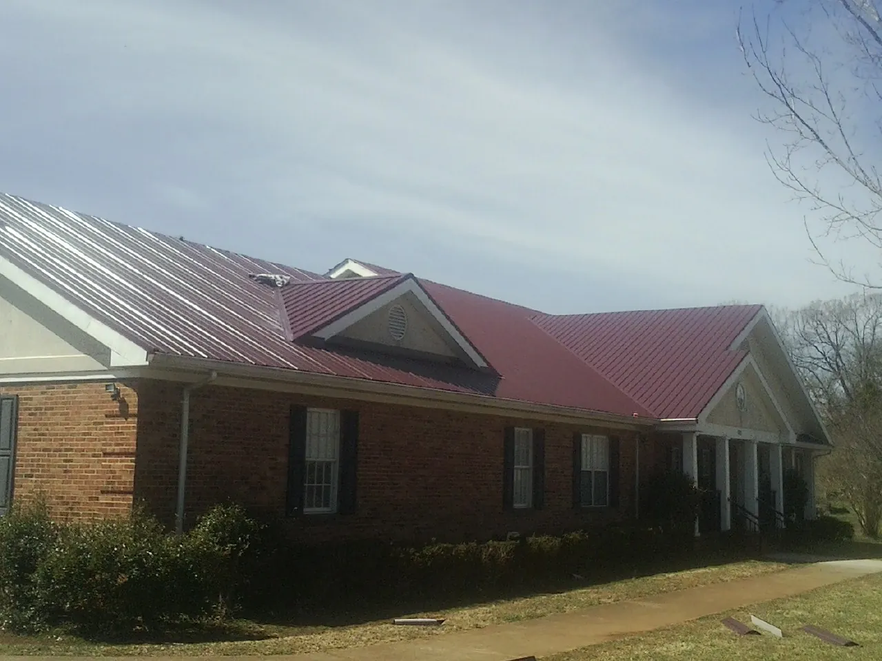 Red metal roof with gabled entries on a long brick building, from a Hail Damage Roof Repair job in Moffit
