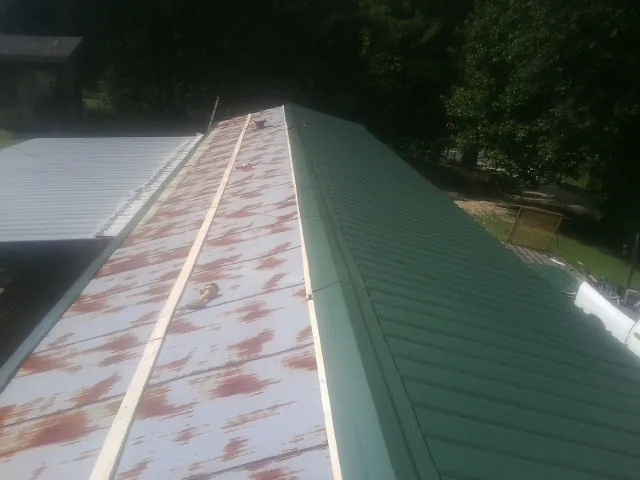 Old rusted panels beside newly installed green metal roofing — Wind Damage Roof Repair by Roofing Brothers in Moffit