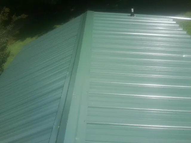 New green metal panels meeting at the ridge of a roof — Flat Roof Repair work by our crew in Moffit
