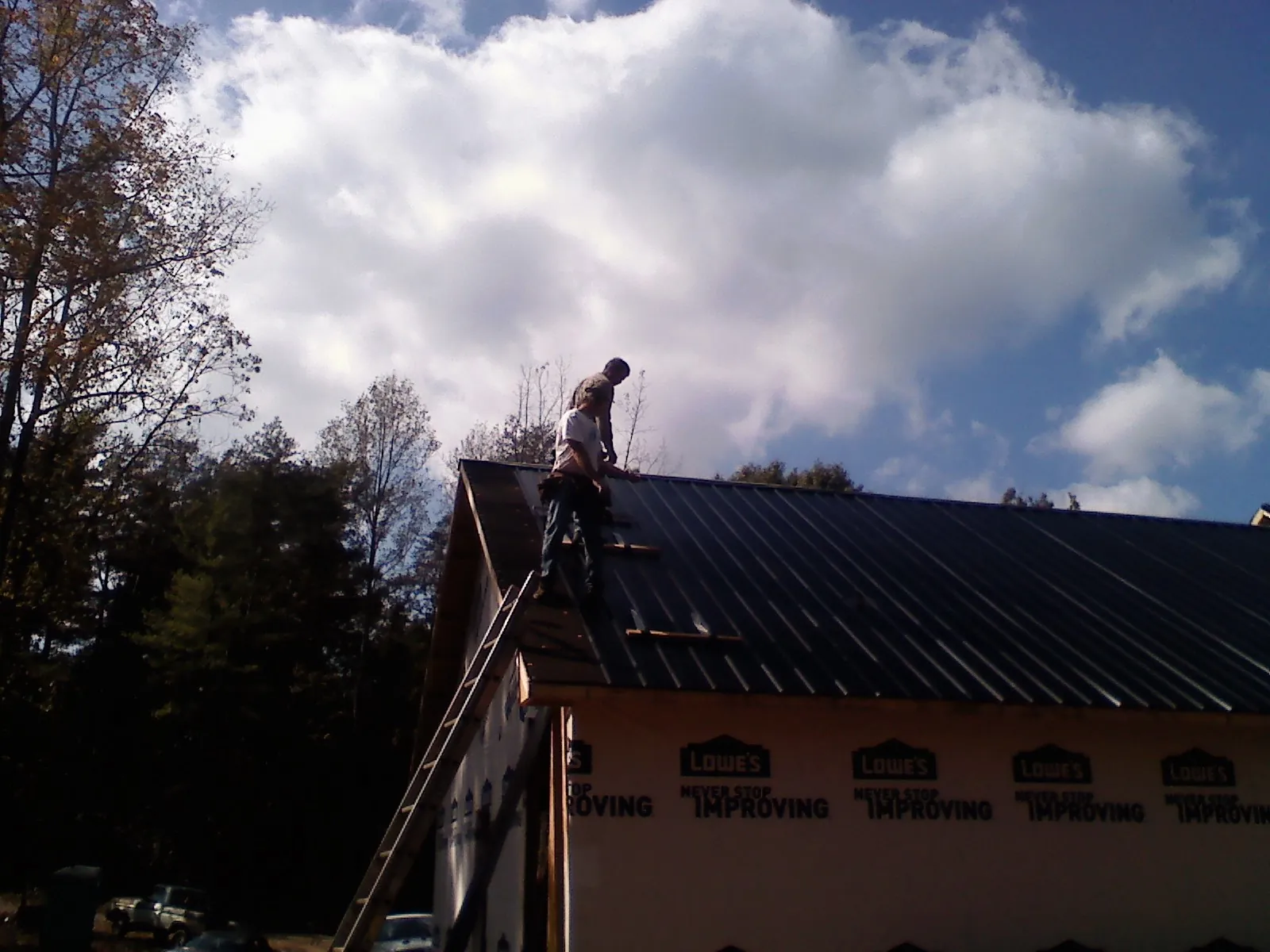 Roofer fastening dark metal panels high against a cloudy sky, from a Roof Inspection job in Moffit