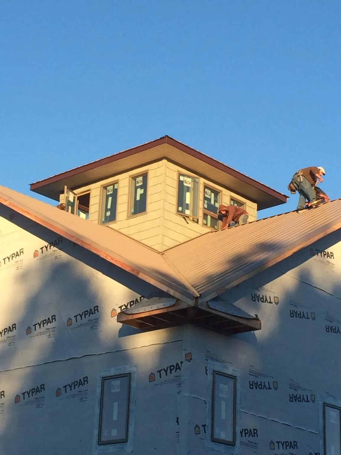 Roofers working around a rooftop cupola on a new metal roof at sunset — Roof Waterproofing in Moffit by Roofing Brothers